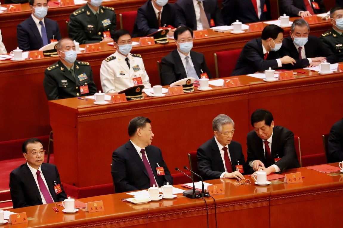 Mientras Li Zhanshu intenta sujetarle las manos, Xi Jinping se vuelve ligeramente hacia atrás y llama a uno de sus asistentes.