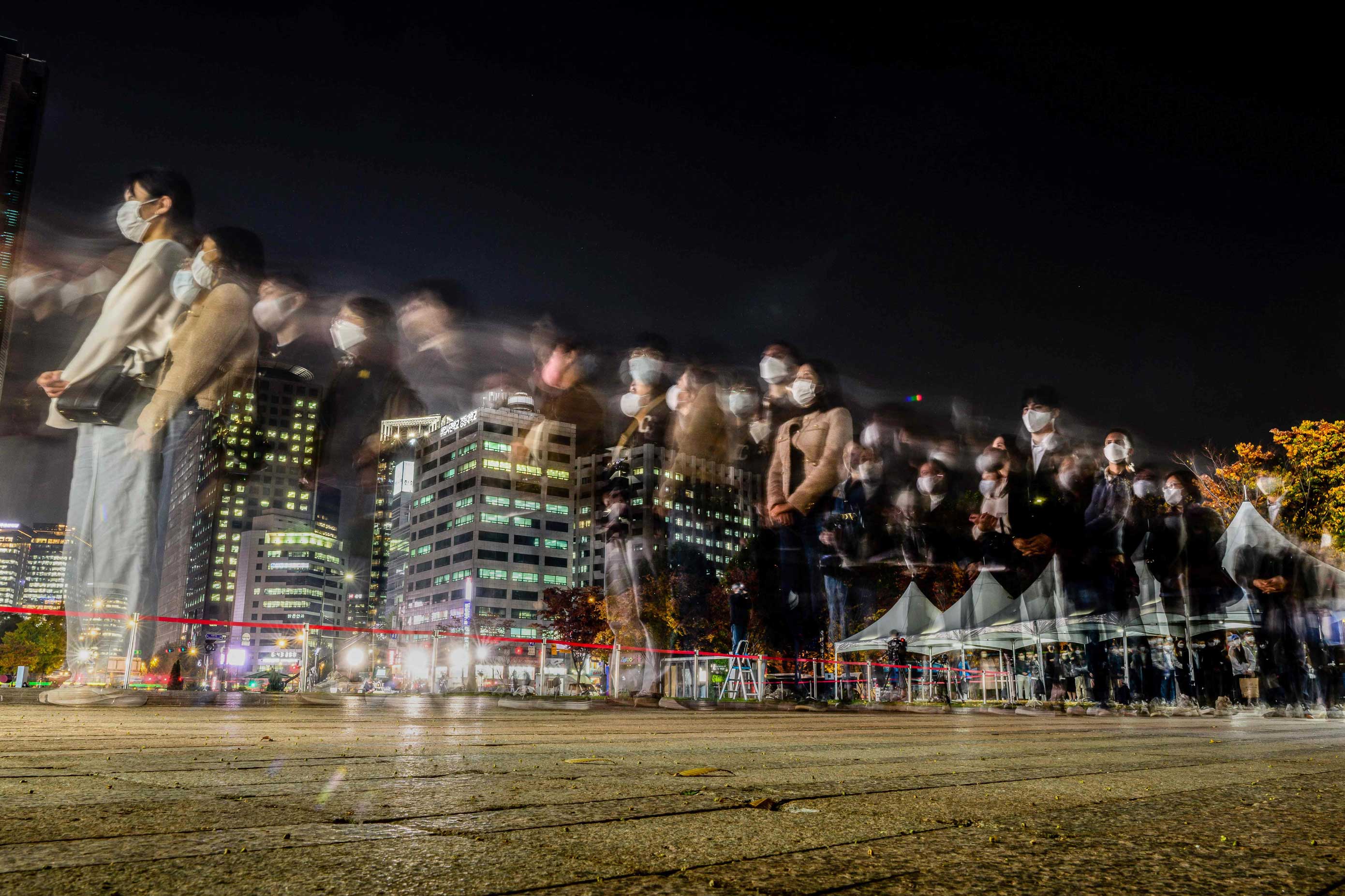 Fotografía de exposición múltiple de la cola de asistentes al homenaje de las victimas