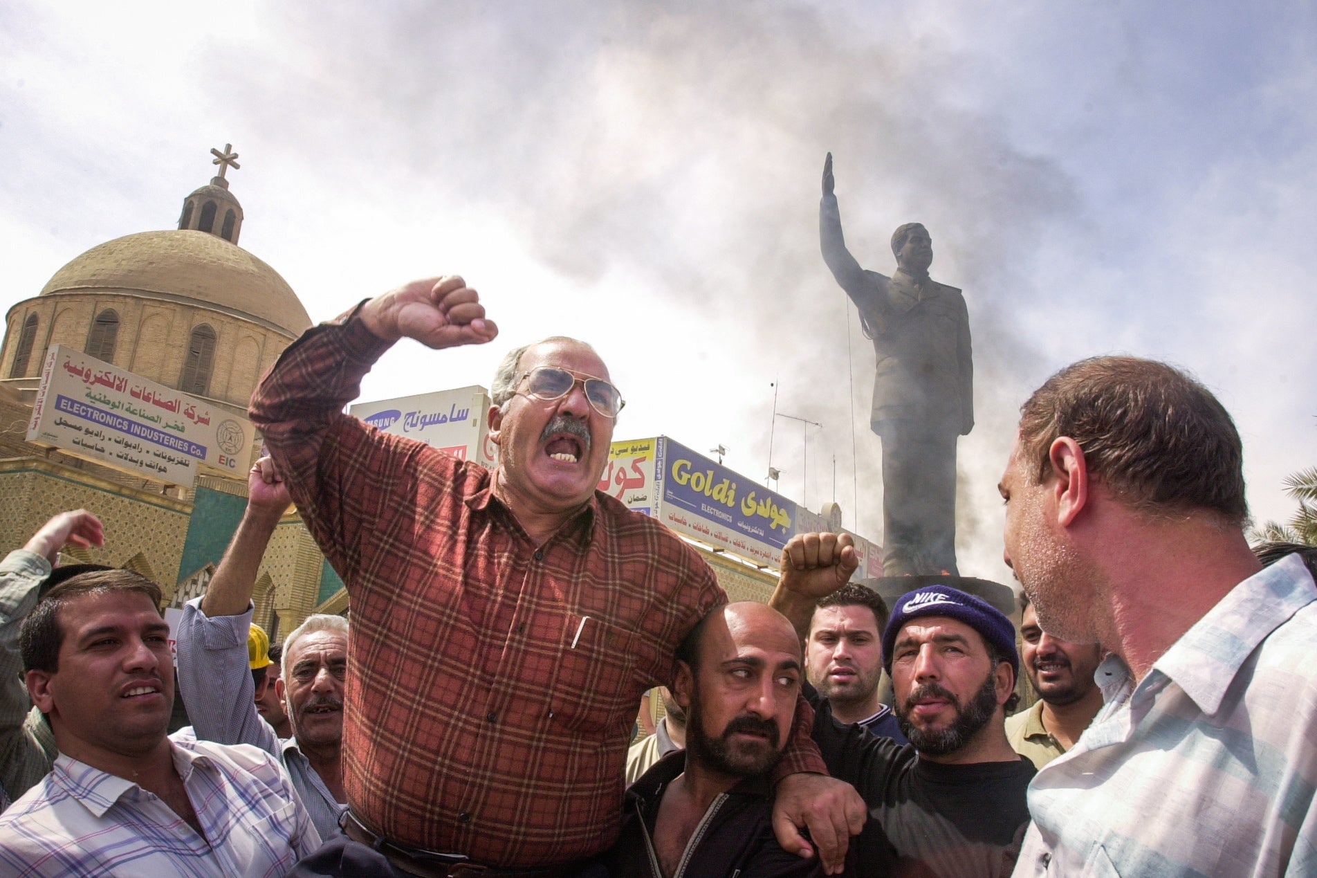 Iraquíes celebran, junto a una gran estatua de Sadam Husein, la toma de control de área de Bagdad por parte del Ejército de EE.UU