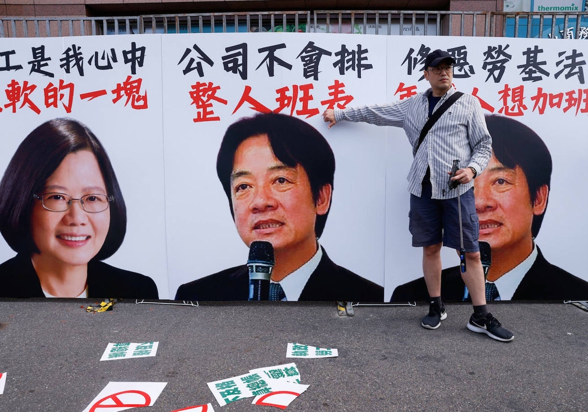 Una persona posa para una foto con el pulgar hacia abajo frente a un cartel de la presidenta de Taiwán, Tsai Ing-wen, y el vicepresidente William Lai durante la marcha anual del Día del Trabajo en Taipei, T