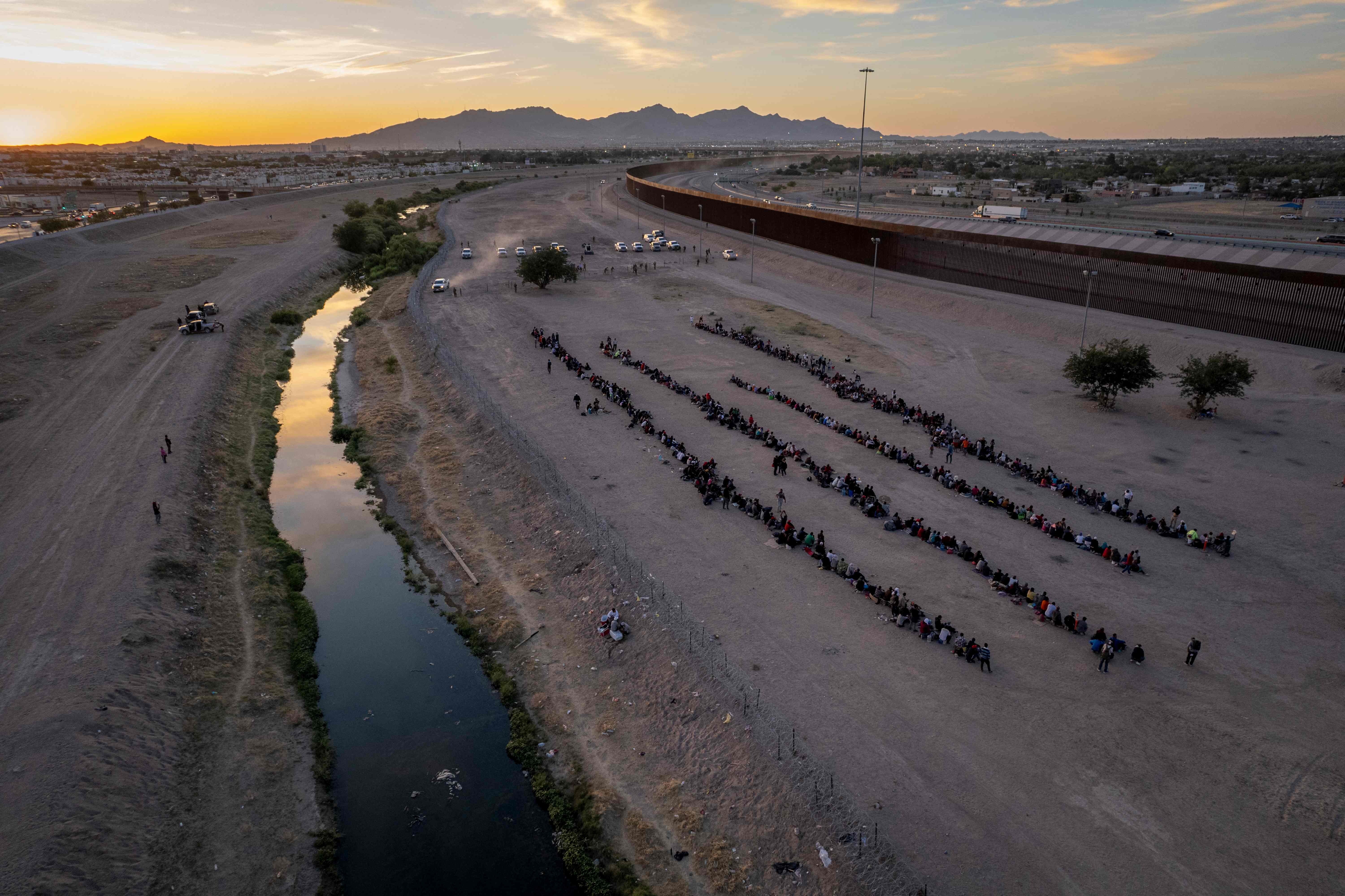 Visto desde una vista aérea, inmigrantes esperan cerca de la valla fronteriza entre EE.UU. y México tras cruzar el Río Grande  desde México