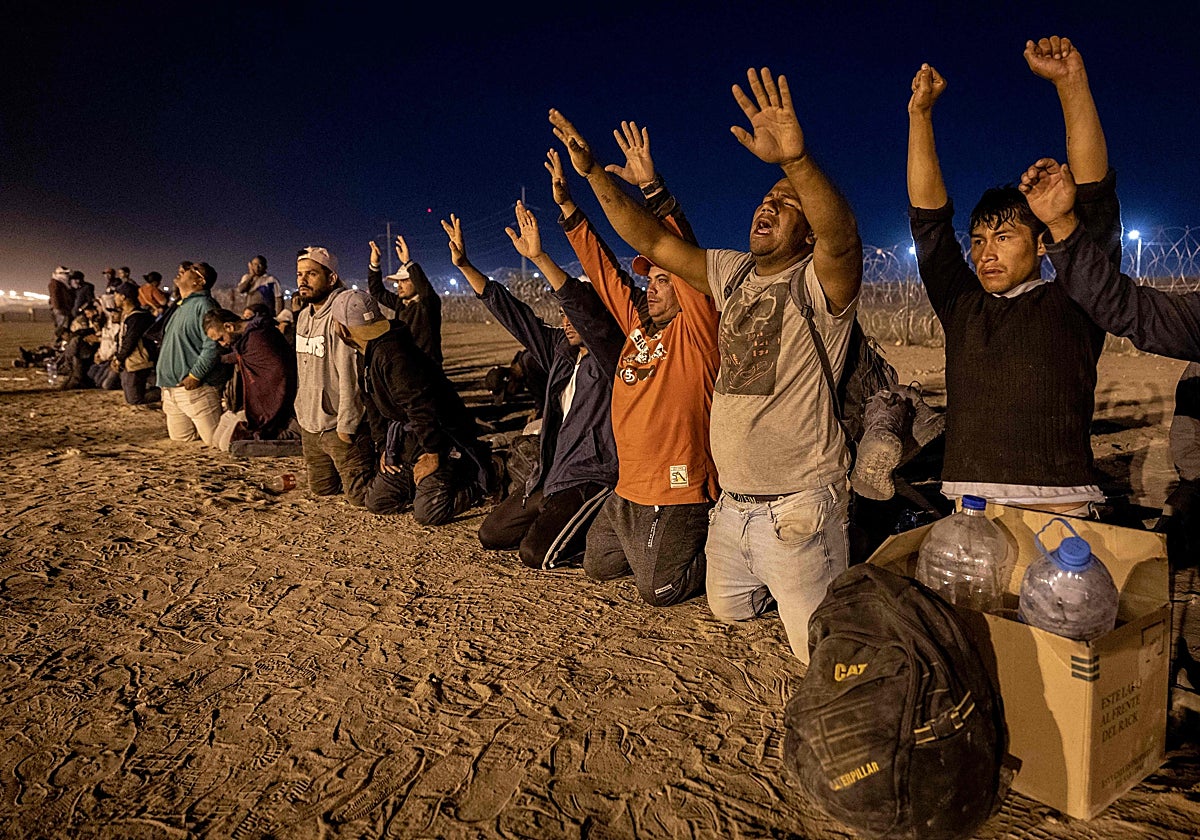 Inmigrantes rezan mientras esperan que los agentes fronterizos estadounidenses les tramiten el asilo tras cruzar desde México