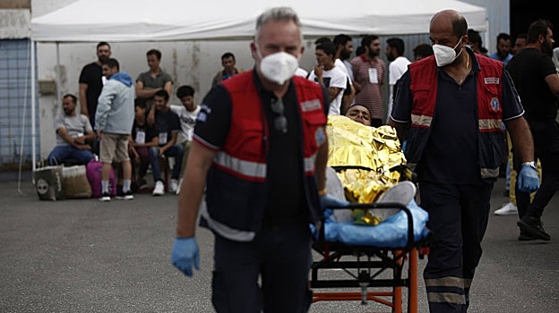 Paramédicos del Servicio Nacional de Ambulancias de Emergencia de Grecia transfieren a un migrante a su ambulancia, en Kalamata