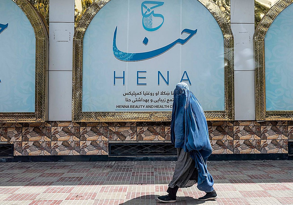 Una mujer afgana vestida con burka pasa por delante de un salón de belleza