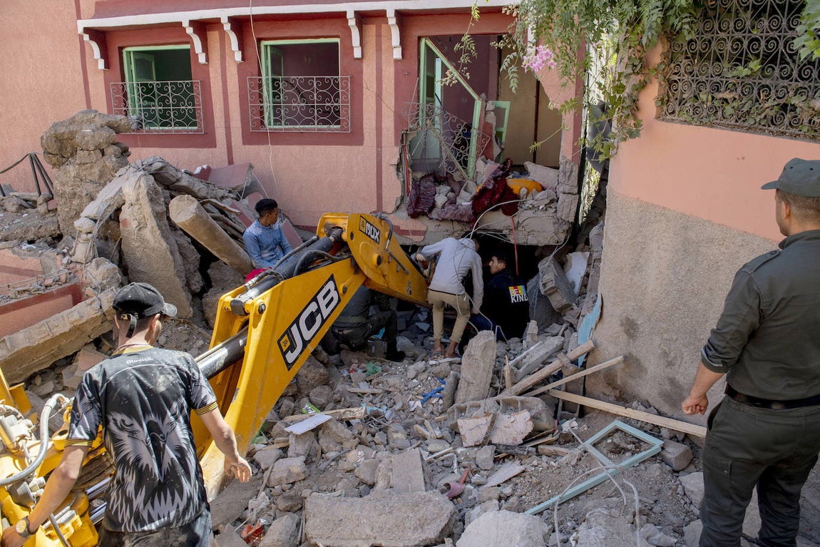Varias personas buscan entre los escombros de un edificio dañado con la ayuda de una excavadora tras el terremoto en Marrakech
