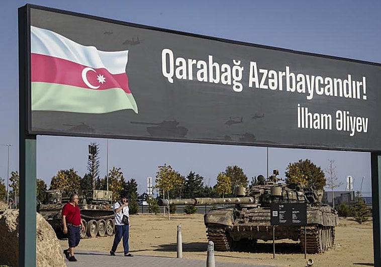 La gente camina junto a un cartel que dice: '¡Karabaj es Azerbaiyán! Ilham Aliev' en el Parque de Trofeos Militares, que contiene trofeos de guerra incautados por las Fuerzas Armadas de Azerbaiyán