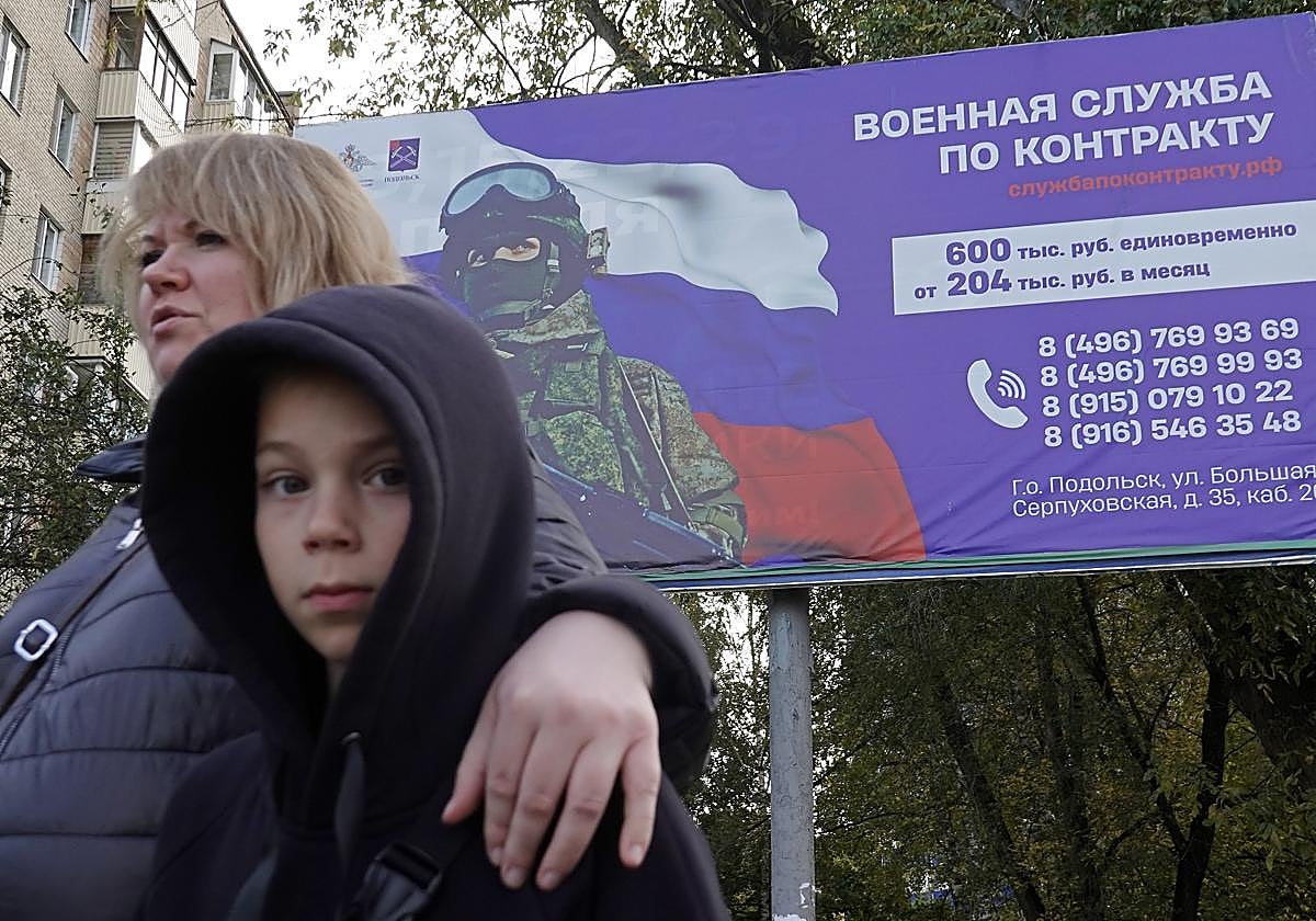 Una mujer caminando con su hijo frente a una pancarta de las Fuerzas Armadas