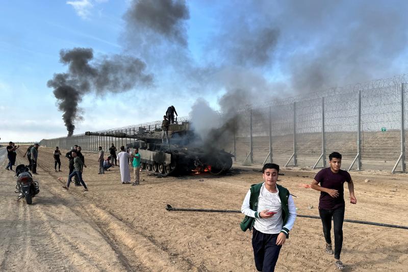 Ppalestinos reaccionan cuando un vehículo militar israelí arde después de ser alcanzado por hombres armados palestinos que se infiltraron en áreas del sur de Israel, en el lado israelí de la frontera entre Israel y Gaza