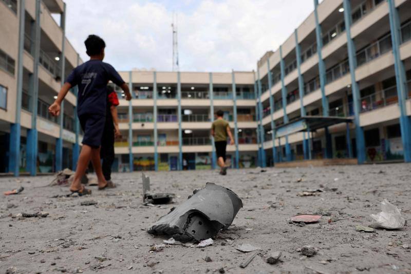 Niños palestinos caminan entre escombros en el patio de una escuela dirigida por la Agencia de Obras Públicas y Socorro de las Naciones Unidas para los Refugiados de Palestina