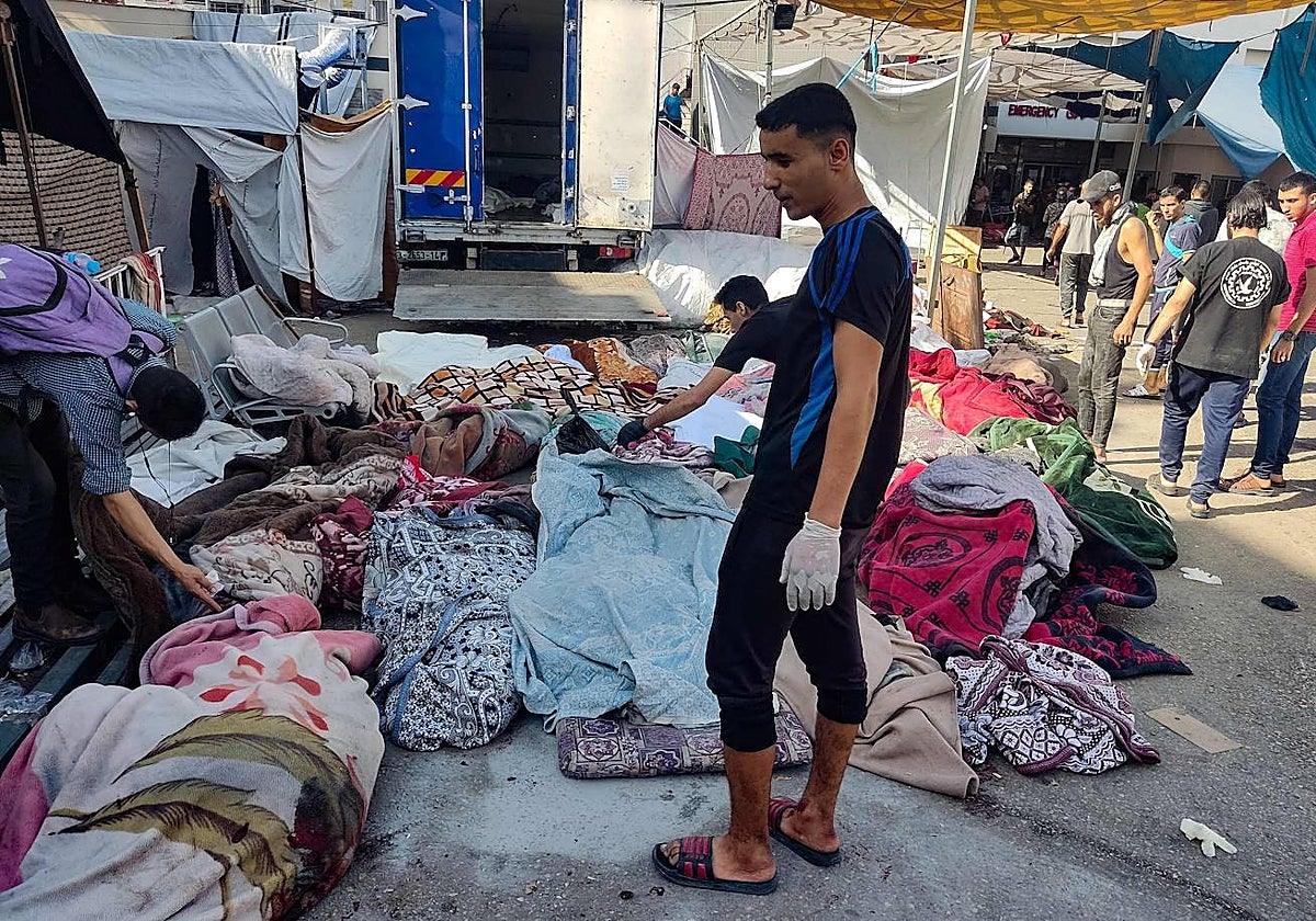 Hombres revisan los cuerpos de las personas muertas en el bombardeo que afectó a una escuela que albergaba a palestinos desplazados, mientras yacían en el suelo en el patio del hospital Al-Shifa