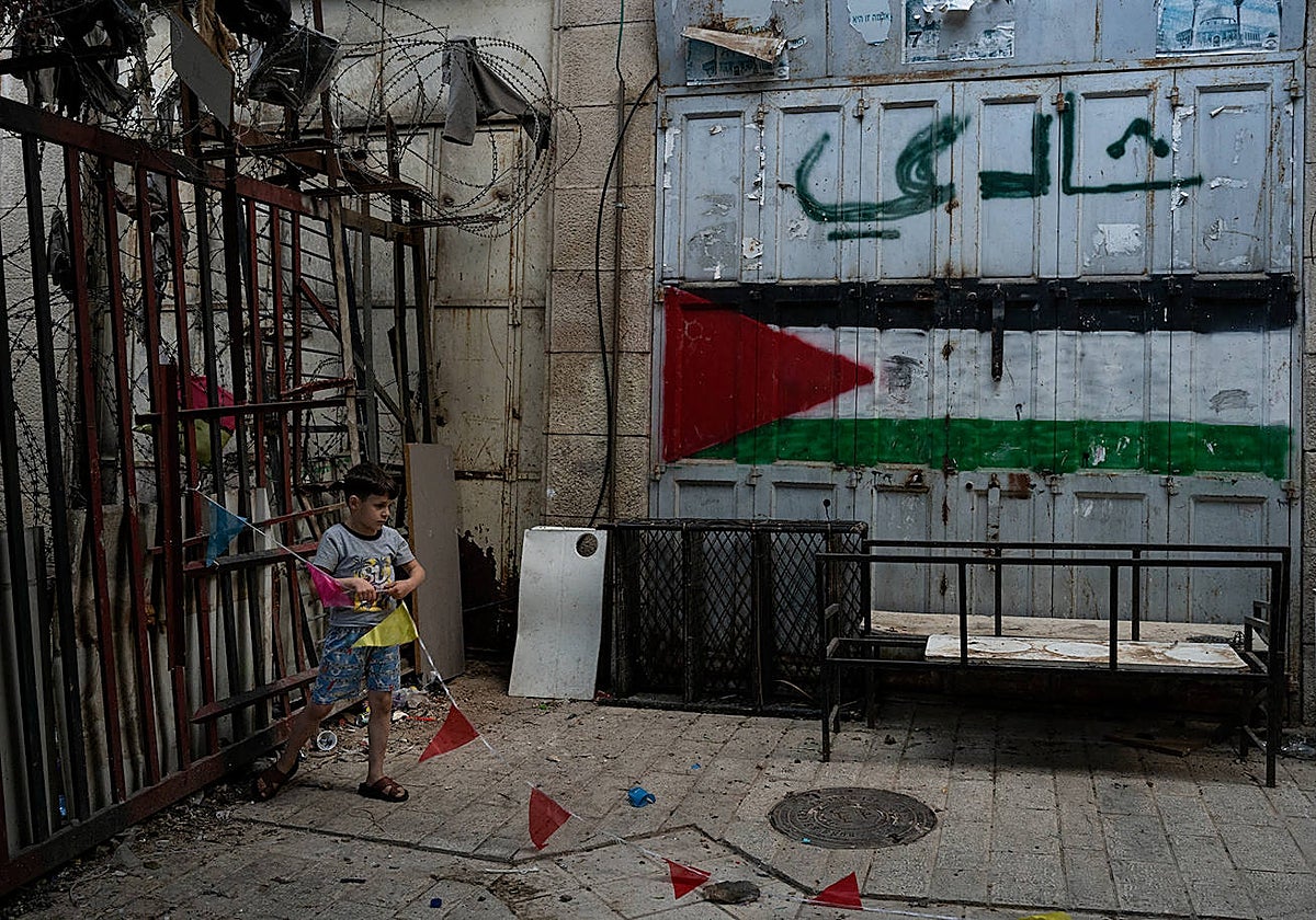 Un niño juega en un callejón de Hebrón junto a una bandera palestina pintada en una puerta
