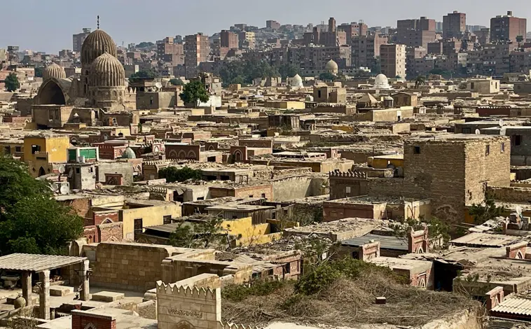 Imagen principal - Los cementerios históricos de El Cairo, donde despuntan sus panteones con las típicas cúpulas bulbosas islámicas, están rodeados de bloques de viviendas y chabolas por el caótico desarrollismo de El Cairo (imagen superior). Muchas de sus tumbas, algunas con siglos de antigüedad, están siendo destruidas para construir avenidas y autopistas elevadas (arriba a la izquierda), mientras que algunos mausoleos se han convertido en infraviviendas (arriba a la derecha). 