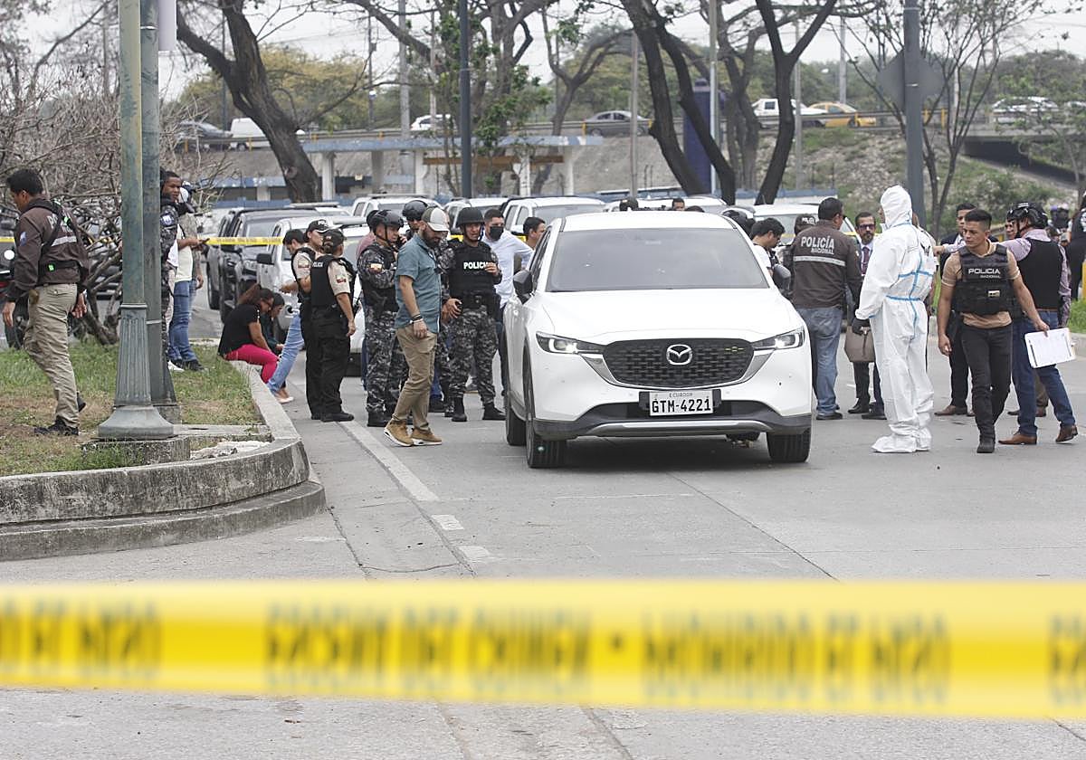 Varios policías investigan el vehículo con impactos de bala en el que se encontraba el fiscal César Suárez