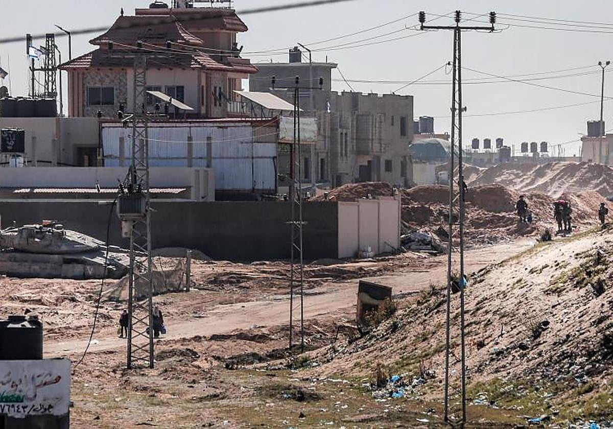 Mujeres palestinas desplazadas que cargan sus pertenencias pasan junto a las fuerzas israelíes mientras huyen del área de la ciudad de Hamad