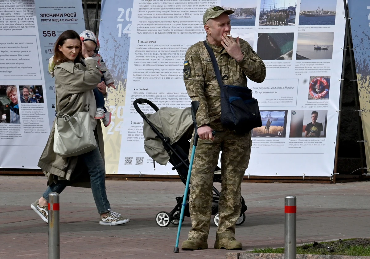 Una mujer camina con un bebé detrás de un militar ucraniano herido, en Kiev