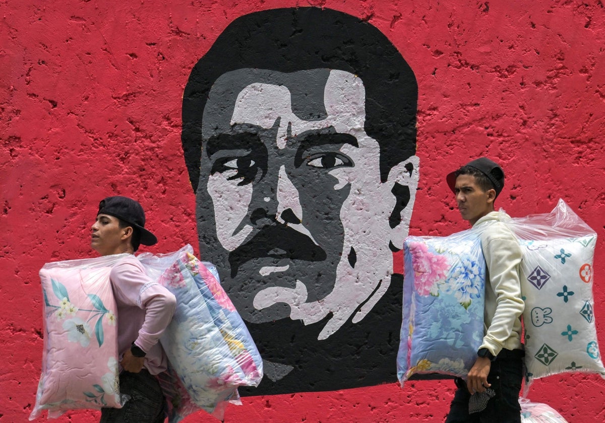 Dos venezolanos pasean por Caracas ante una pintada de Nicolás Maduro