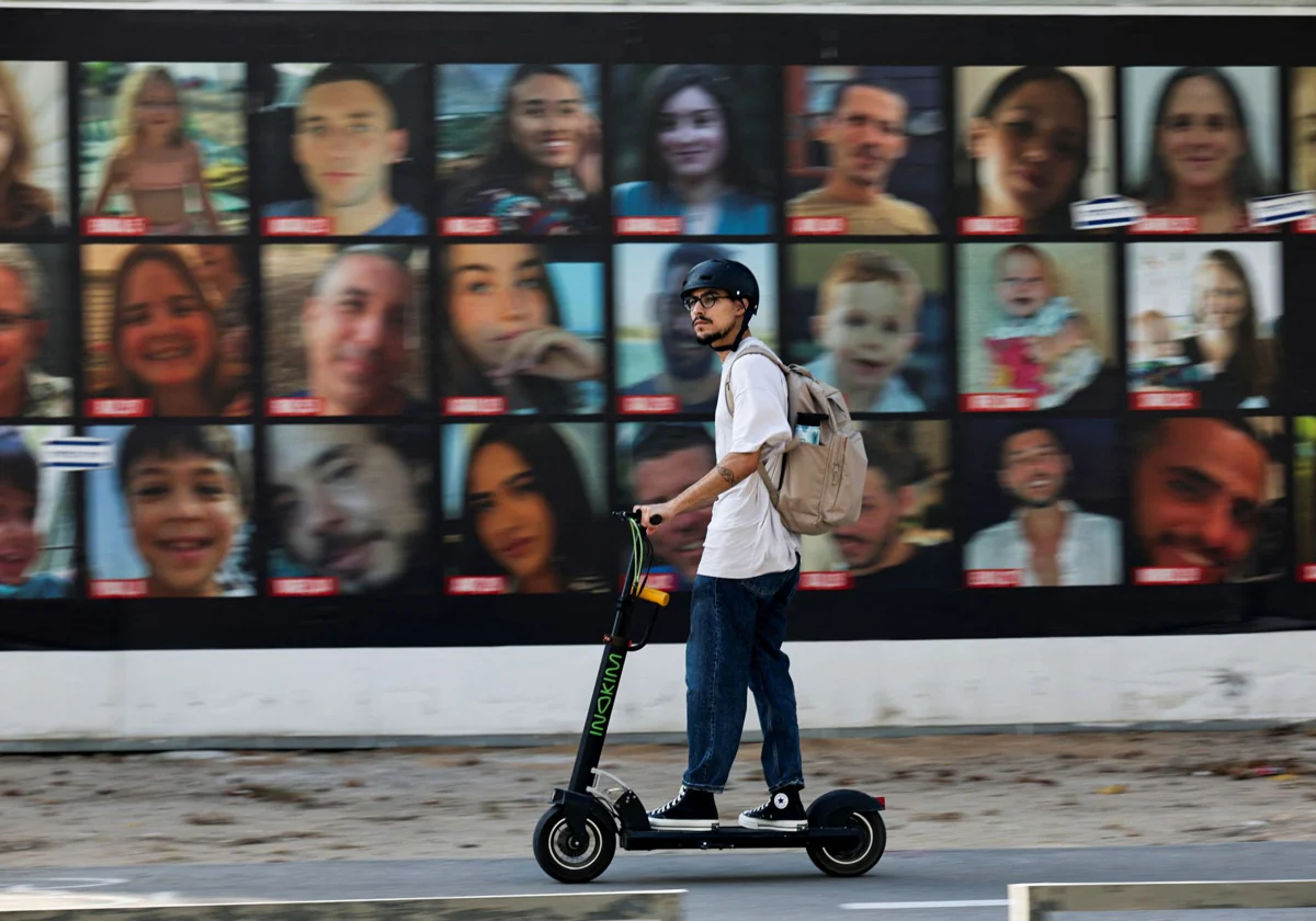 Un hombre pasa en una scooter junto a fotografías de rehenes secuestrados durante el mortal ataque del 7 de octubre por parte del grupo islamista palestino Hamas, en Tel Aviv