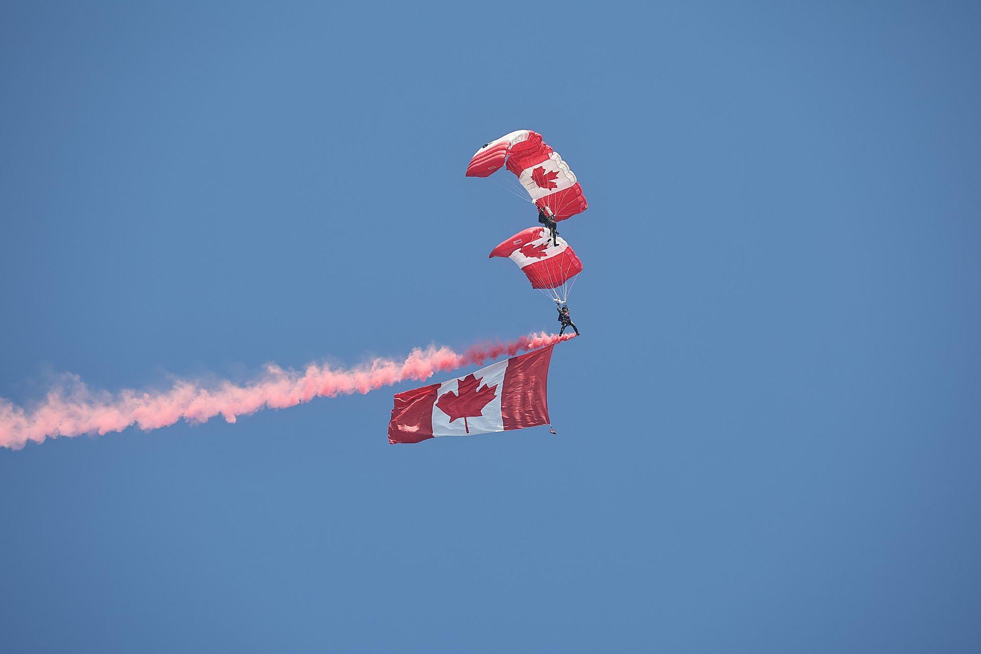 Paracaidistas acrobáticos canadienses portan la bandera nacional por los cielos de Normandía en la playa de Juno, Courseulles-sur-Mer.