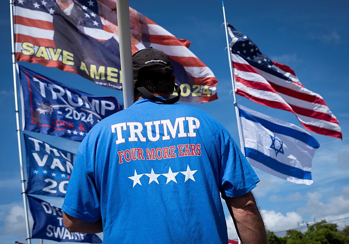 La persona se encuentra frente a banderas mientras la gente espera a que pase la caravana del Primer Ministro israelí, Benjamin Netanyahu