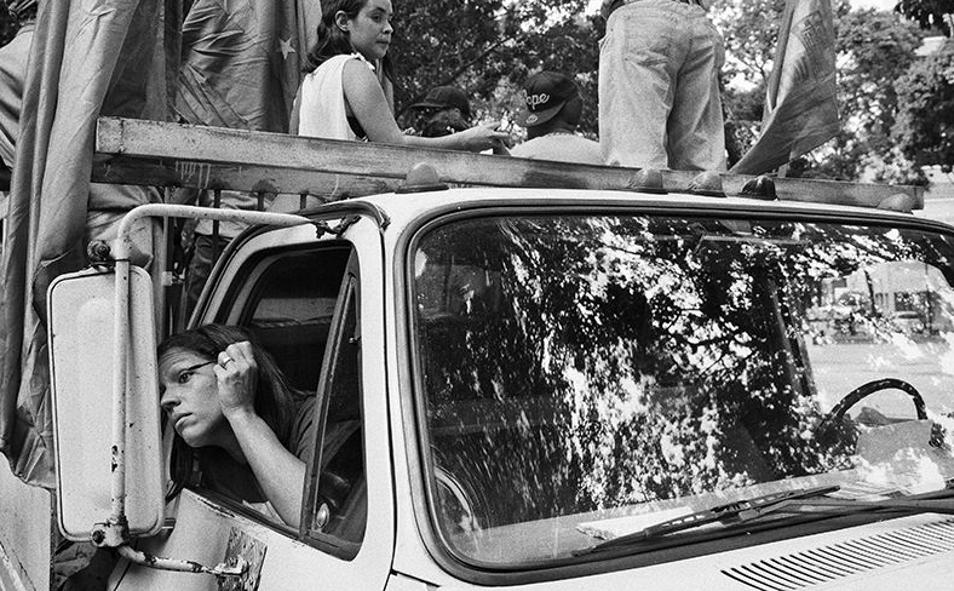 Imagen principal - Caracas, noviembre de 2015. Una mujer se maquilla en el interior de un vehículo mientras espera el inicio de un acto electoral de la venezolana (foto superior). Debajo: Cúcuta (Colombia), febrero de 2019. Dos emigrantes venezolanas siguen desde sus teléfonos móviles las noticias que llegan desde Venezuela en relación a la crisis venezolana. Tachira (Venezuela), febrero de 2019. Una bandera venezolana yace destruida en el suelo tras una manifestación pacífica de la oposición venezolana que terminó cuando fue dispersada por las fuerzas de seguridad del régimen con fuertes enfrentamientos con la Guardia Nacional Bolivariana