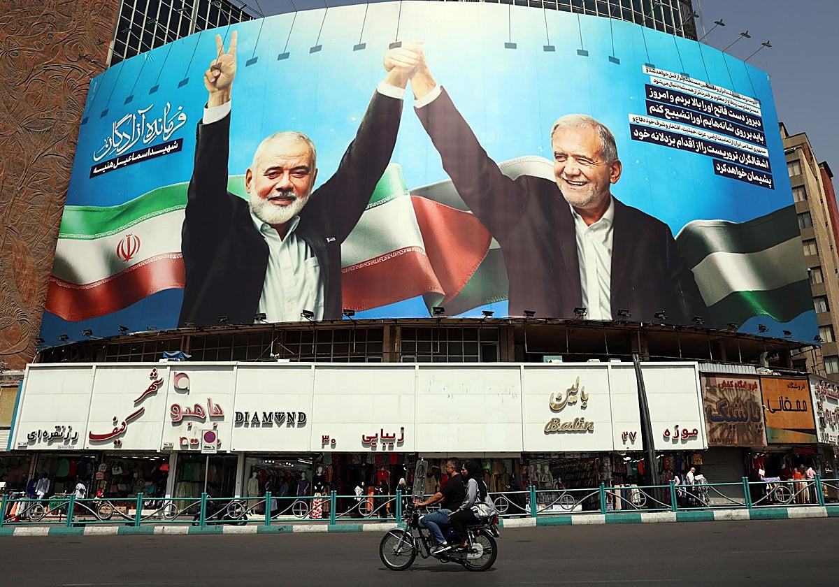 - Iraníes pasan en coche frente a una valla publicitaria que representa al presidente iraní Masoud Pezeshkian (d) y al difunto líder de Hamás Ismail Haniyeh, en la plaza Valiasr de Teherán, Irán