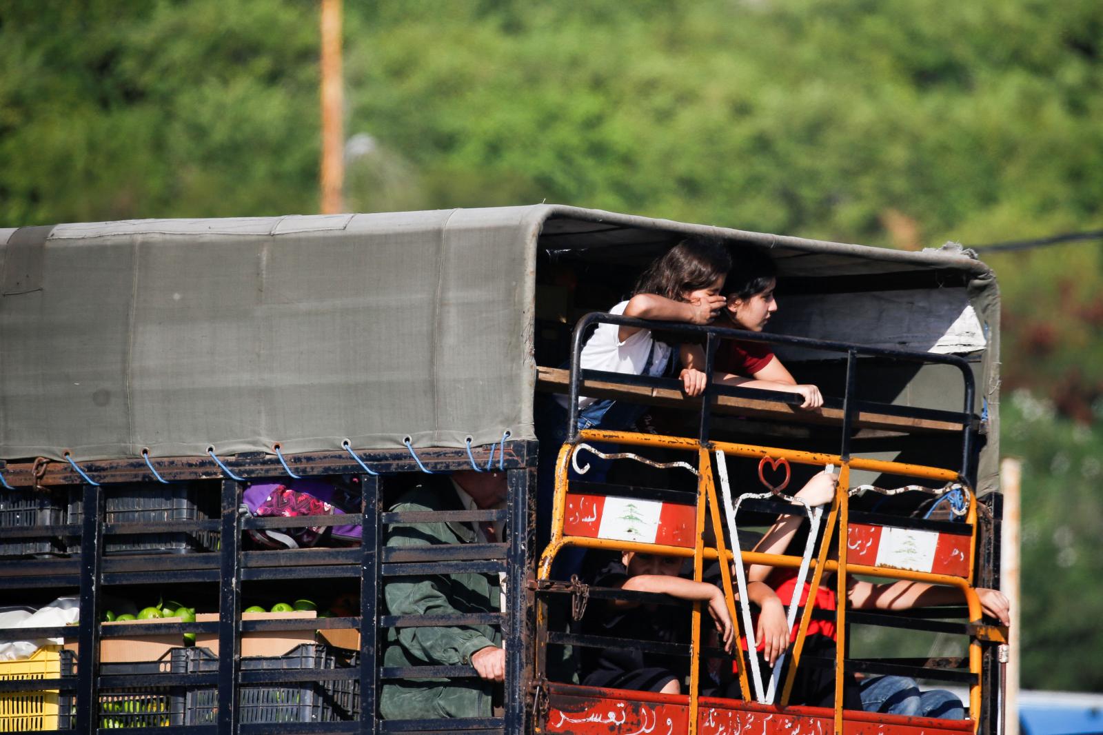 Dos niños asomándose a través de una mirilla del camión donde están siendo desplazados junto a sus pertenencias
