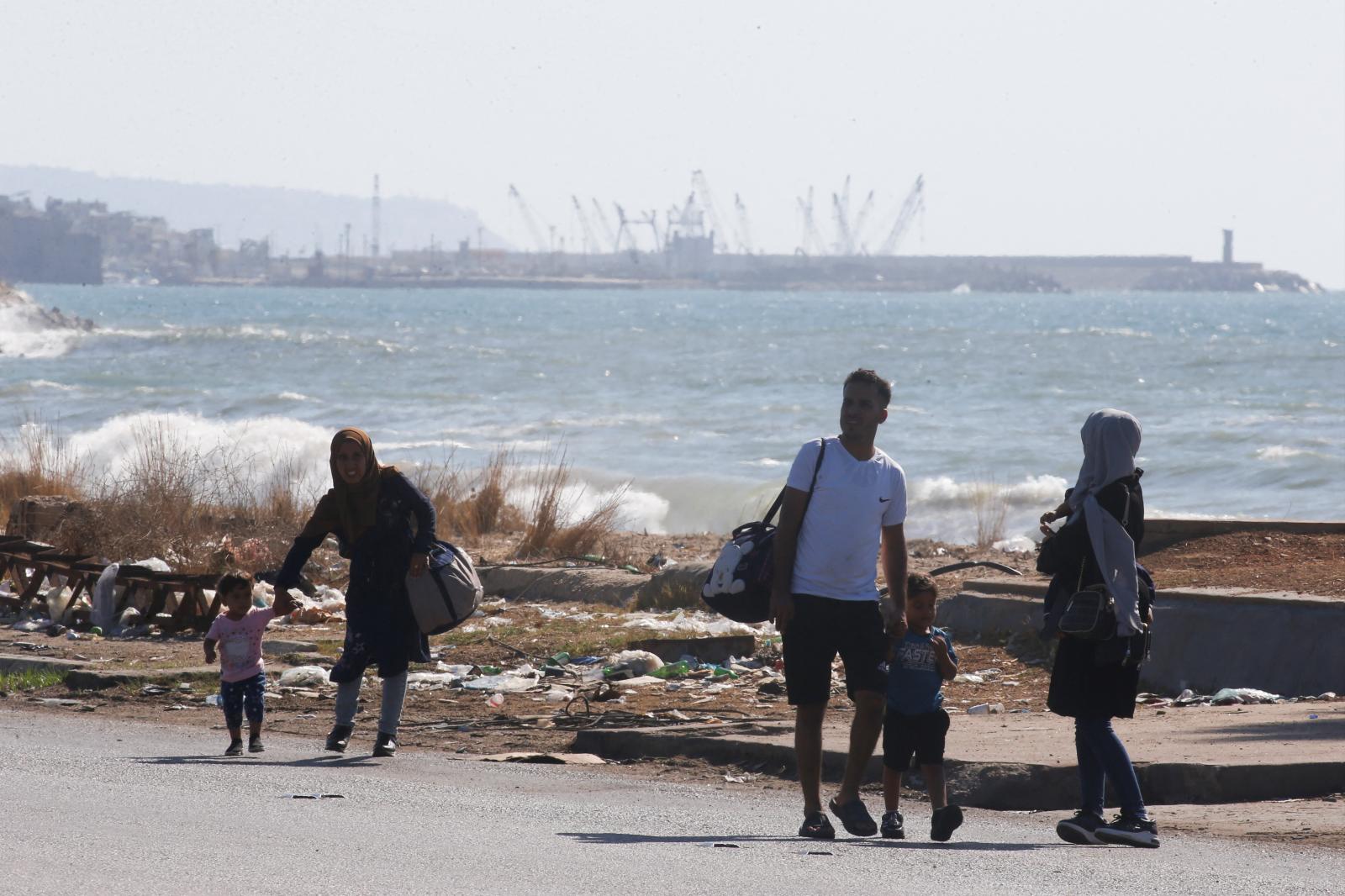 Varias personas desplazándose con sus pertenencias por una playa mientras huyen