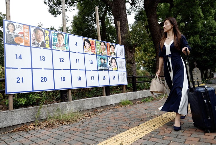 Una mujer camina junto a un cartel con carteles de campaña de candidatos a las próximas elecciones generales en Tokio