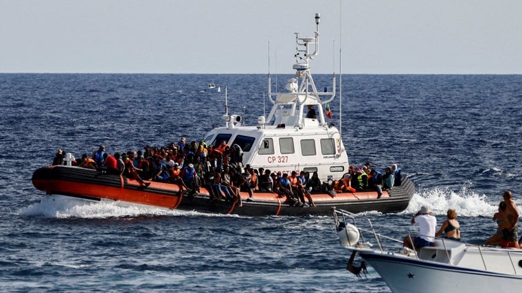 Un barco de la Guardia Costera italiana que transportaba migrantes rescatados en el mar pasa cerca de un barco turístico, en la isla siciliana de Lampedusa