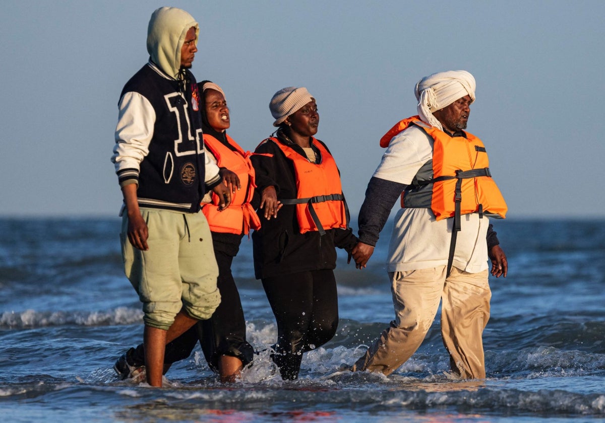 Migrantes caminan por el agua para abordar la embarcación de un traficante e intentan cruzar el Canal de la Mancha frente a la playa de Gravelines,