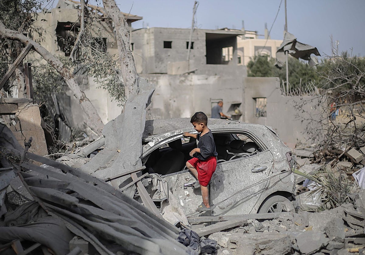 Un niño palestino revisa los restos de un coche entre los escombros de una vivienda en Deir el-Balah