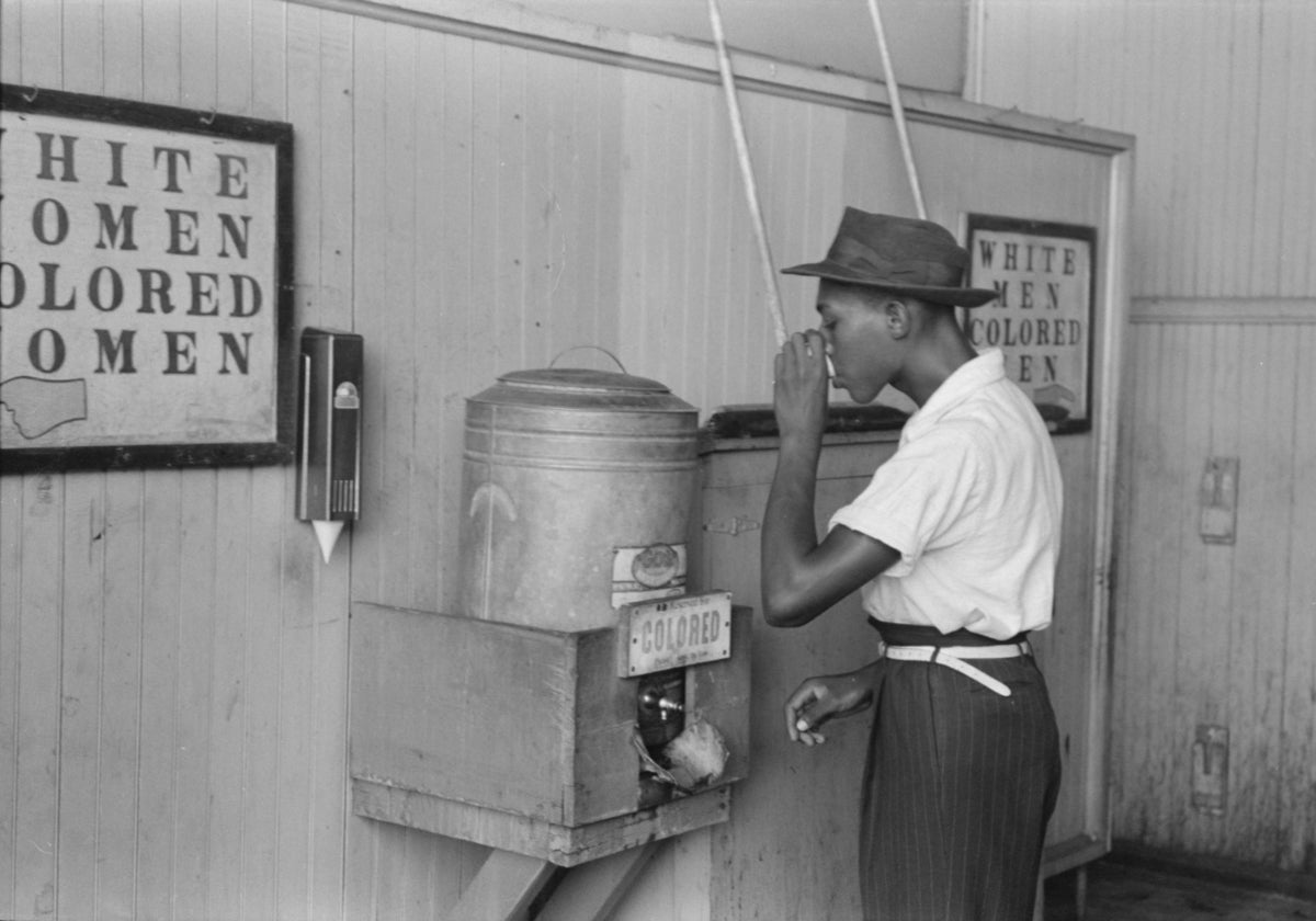 Un joven negro bebe agua en un dispensador separado del que estaba reservado solo para blancos