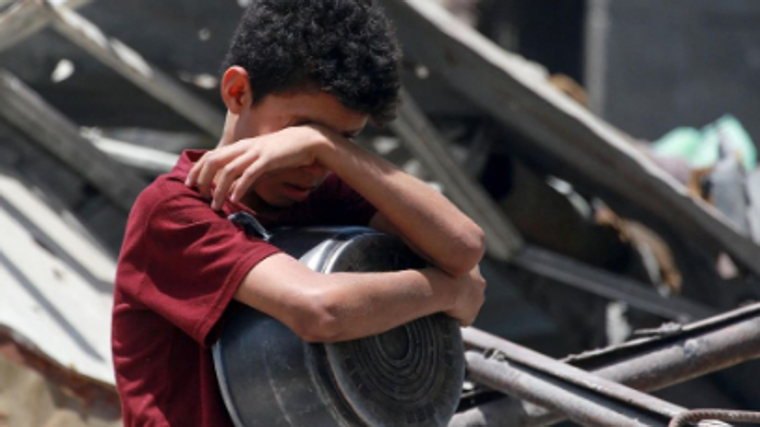 Un niño hace un gesto mientras palestinos desplazados recogen porciones de comida cocinada en una distribución benéfica