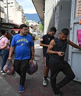 Imagen secundaria 2 - Arriba, la gente carga sus teléfonos tras un apagón en su barrio después de que Estados Unidos atacara Venezuela y capturara a Maduro; debajo a la izquierda, un hombre rescata pertenencias de entre los escombros después del ataque; a la derecha, se puede apreciar cierta normalidad en las calles de Caracas
