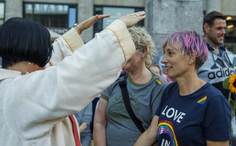 Imagen principal - Arriba, una mujer, revestida con un alba, imparte la bendición a una pareja de mujeres. Debajo, en la concentración también han participado grupos de extrema izquierda que recriminaban a los gays su cercanía a la Iglesia católica. A la derecha, la plaza frente a la catedral se ha llenado de simbología del colectivo LGTBI.