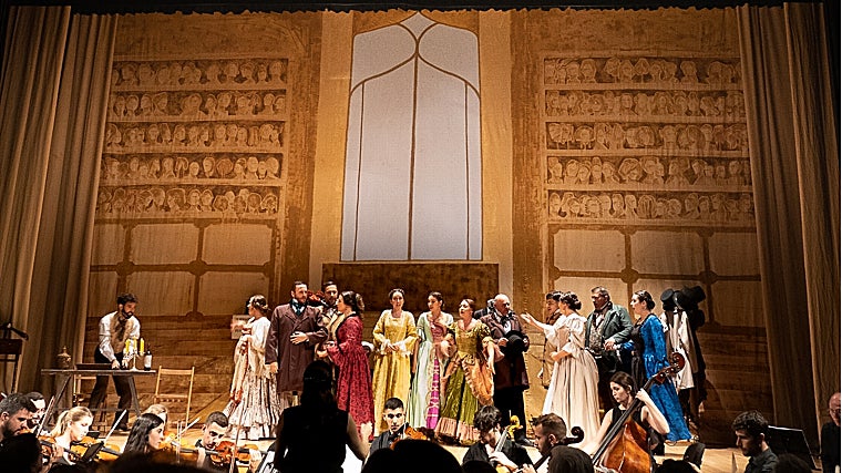 Andrés Merino (izquierda), la silueta de la directora Elena Martínez casi en el centro, y el coro ante el telón de las 157 pelucas