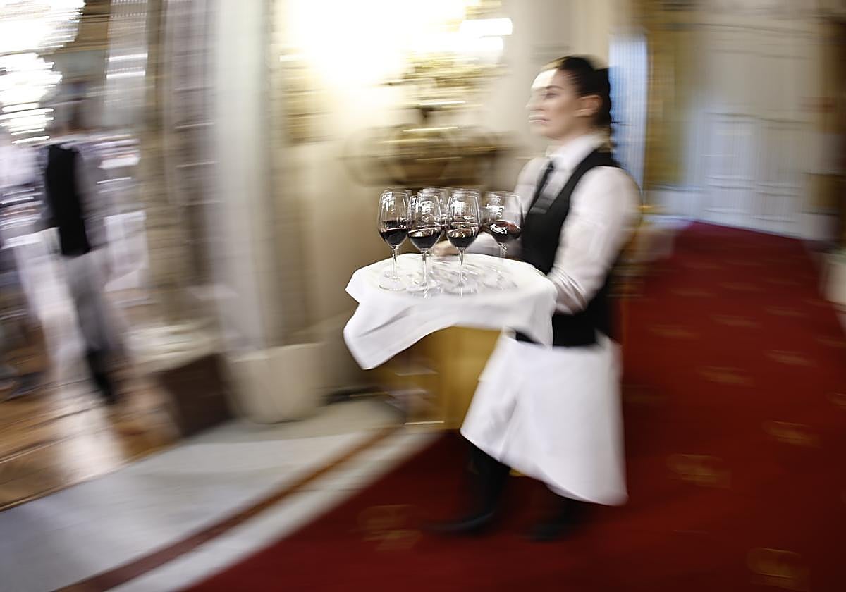 Una camarera lleva varias copas de vino en una bandeja.