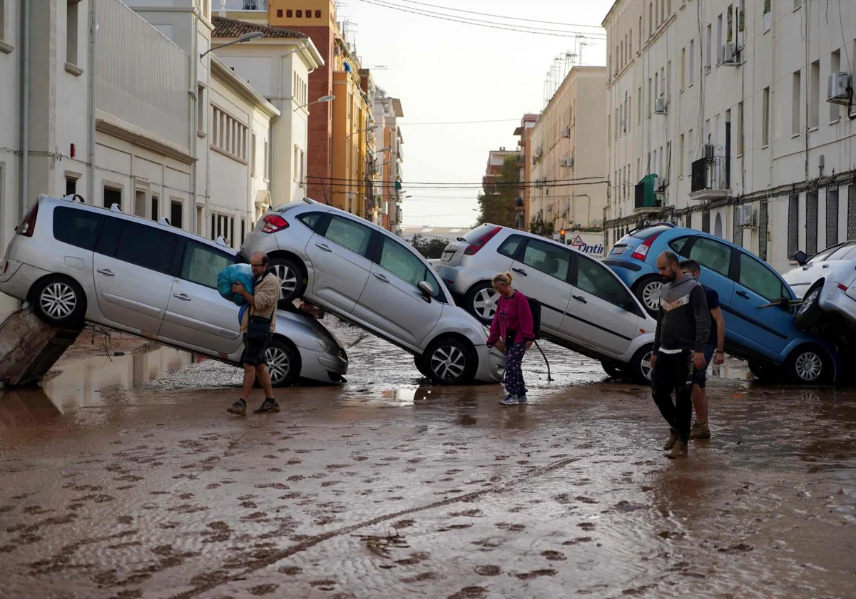 Vecinos pasan junto a coches amontonados tras las mortales inundaciones en el barrio de De La Torre de Valencia