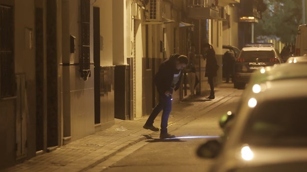 Un agente revisa con su linterna la calle donde se registró el tiroteo; al fondo una compañera habla con una vecina
