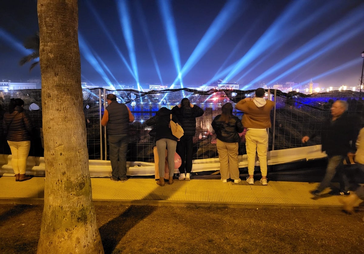Varias personas se asoman por los agujeros que han abierto en las vallas para ver el mapping del río
