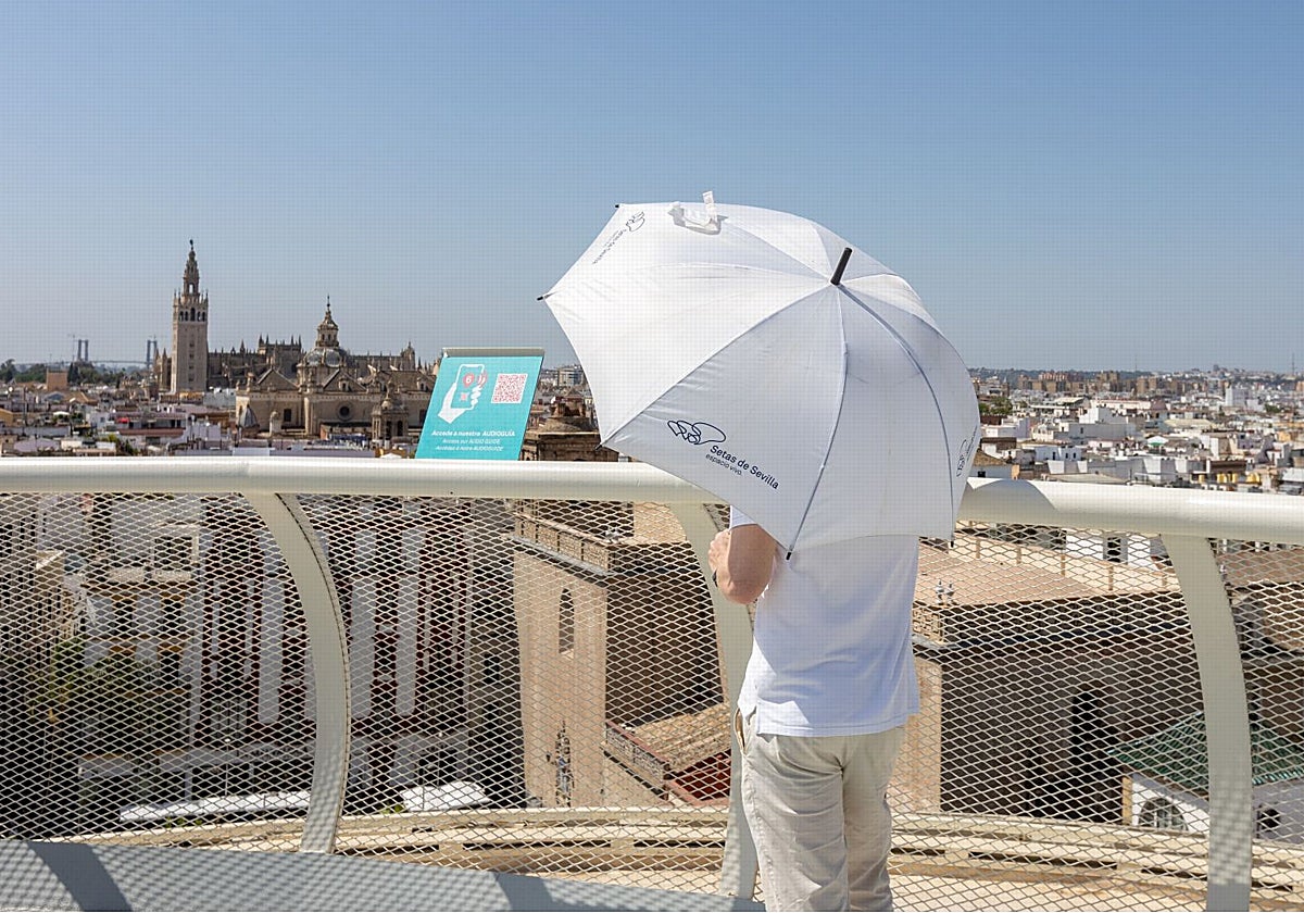 Los turistas hacen uso de paraguas contra el sol durante la visita al mirador de las Setas