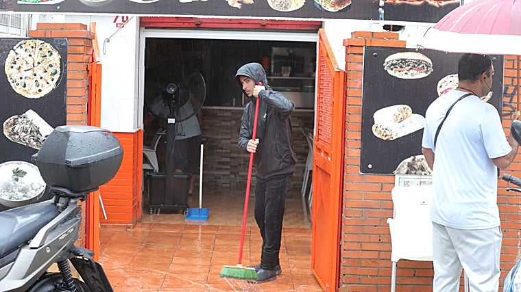 Un trabajador barre hacia la calle el agua que ha entrado en su negocio por las inundaciones que han provocado las lluvias en Sevilla
