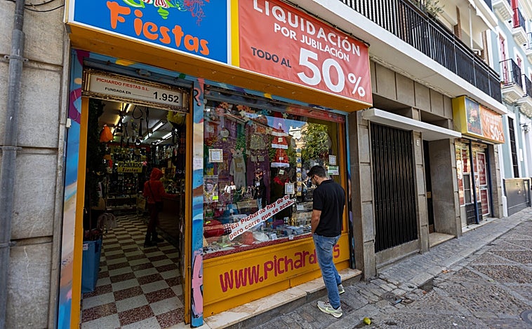 Imagen principal - Arriba, un hombre observa la vitrina de la tienda de disfraces Pichardo, en la plaza Fernando de Herrera; abajo, a la izquierda, la cristalera de Cuadro en Alcaicería de la Loza, vía en la que también ha echado el cierre la tienda de complementos de Antonio Hierro, a la derecha 