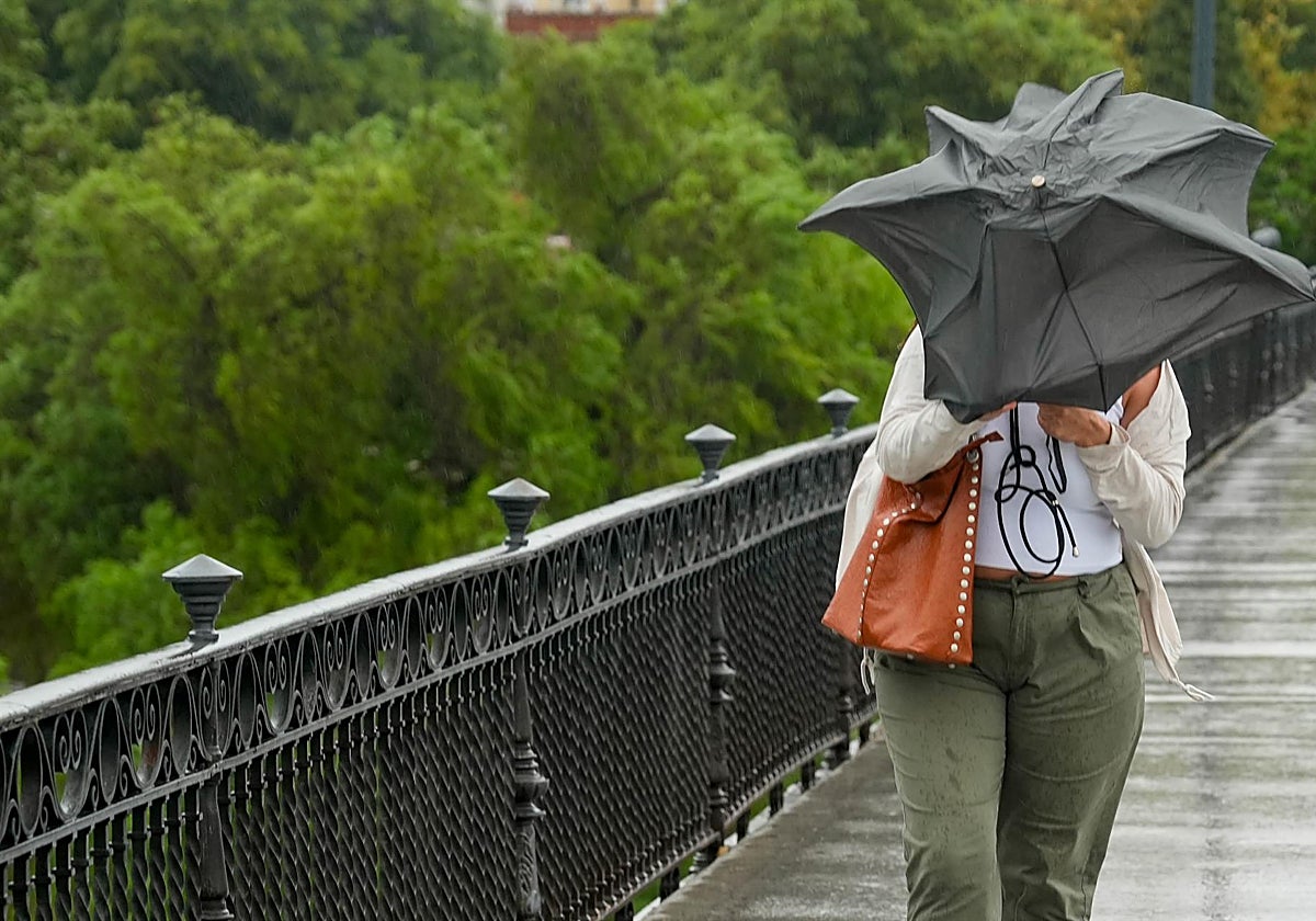 Una mujer atraviesa el puente de Triana bajo la lluvia