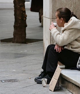 Imagem Secundária 2. Acima: Mulher sentada no chão coberta por um cobertor; Abaixo, na praça, está sentado um homem com a cabeça baixa e à direita está outra mulher implorando. 