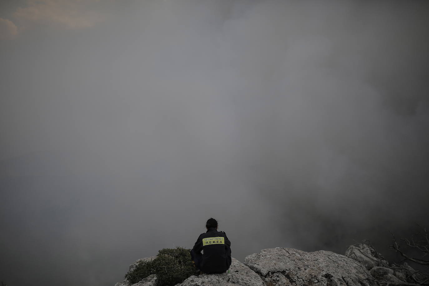 Un bombero se sienta en la cima de la montaña Parnitha, con vistas a un incendio forestal en las afueras de Atenas (Grecia)