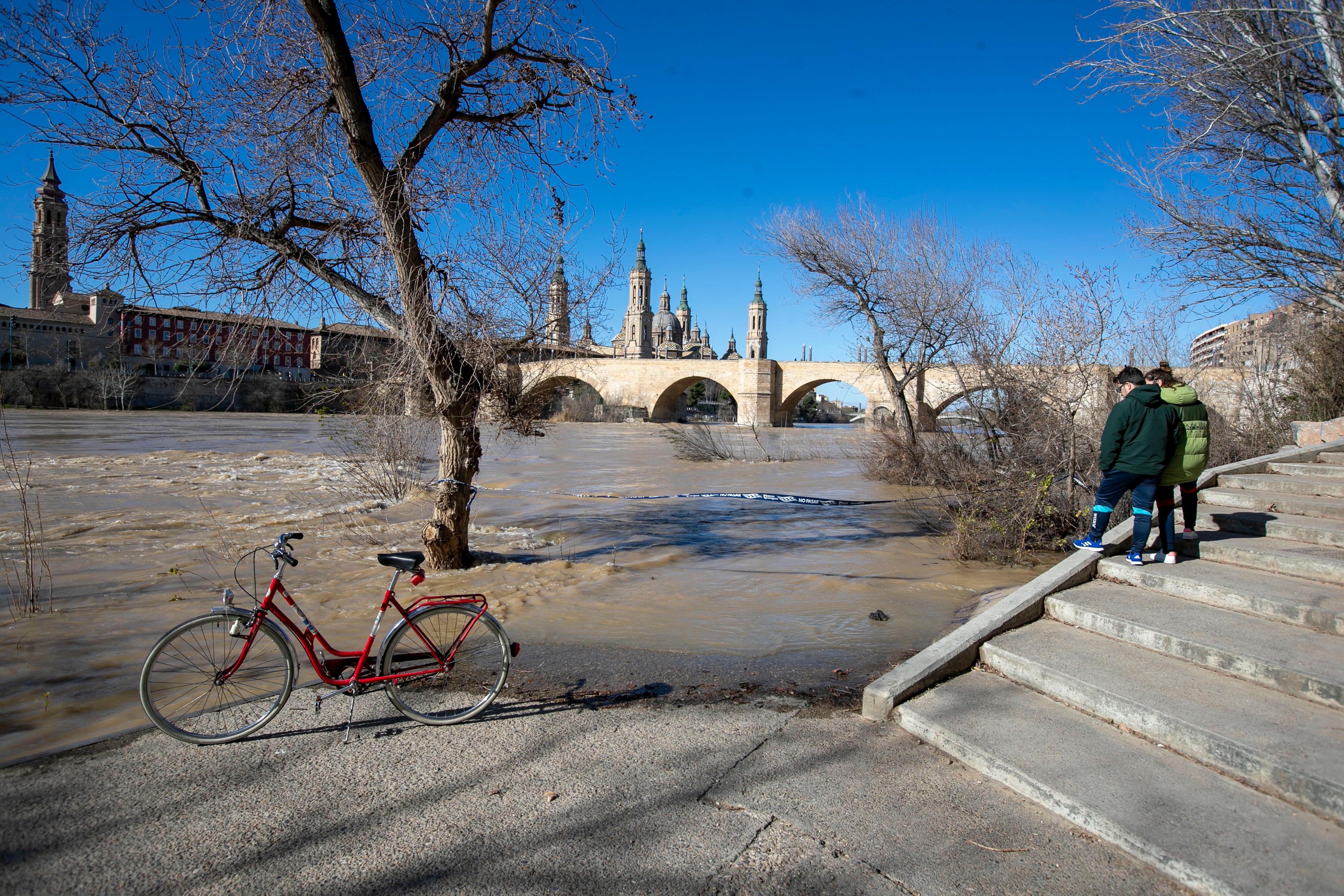 Dos personas observan la crecida del río Ebro a su paso por Zaragoza.