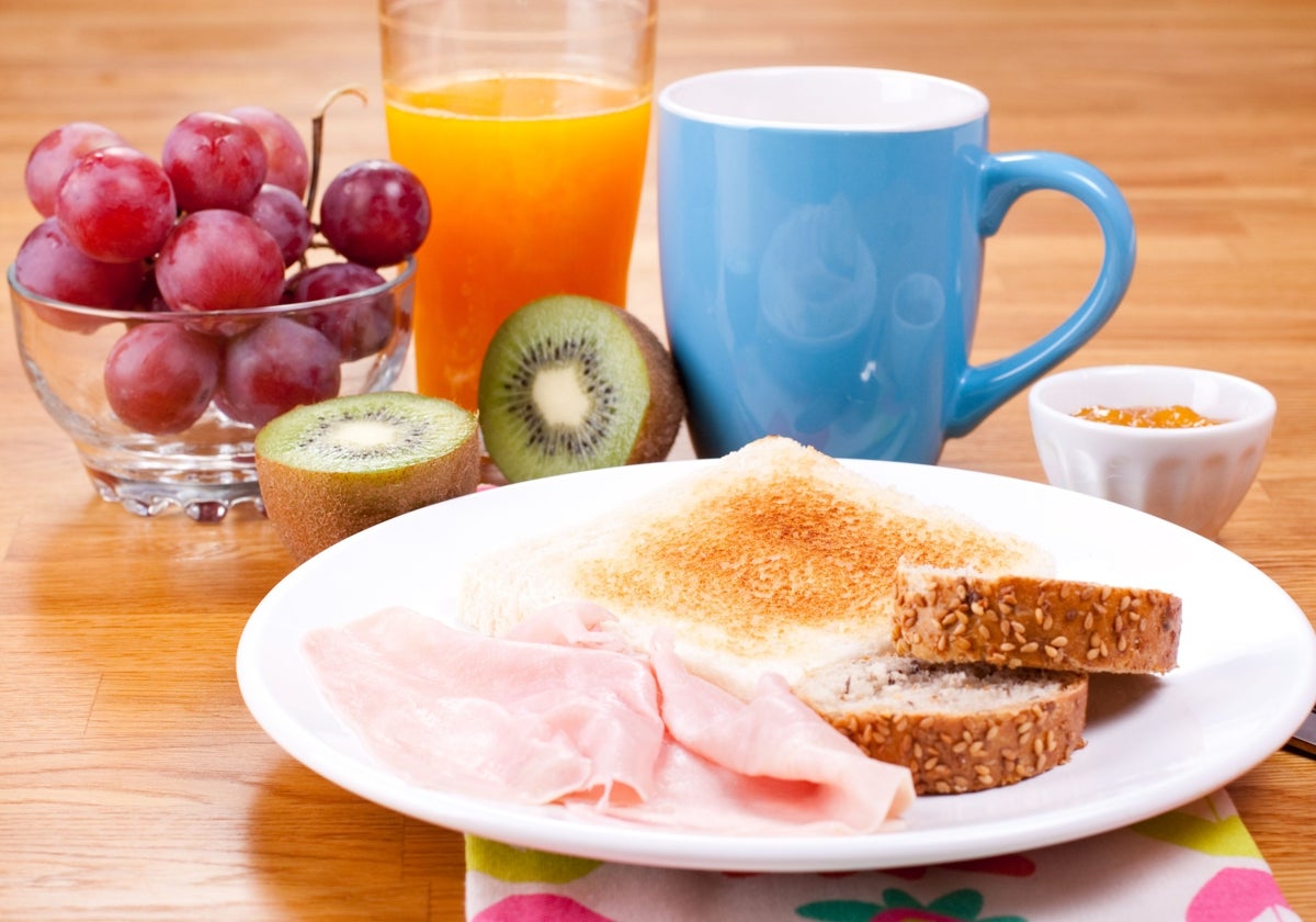 Un desayuno con zumo, café, mermelada, frutas y tostada