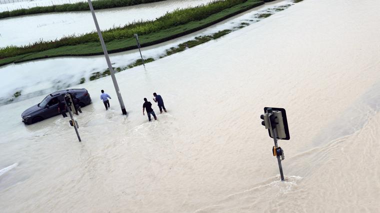 Varias personas tratan de caminar por una carretera inundada en Dubái.