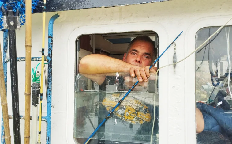 Imagen principal - Arriba, Torrente, en la ventana de su barco. Abajo, un pescador sostiene una serreta, una especie rara hasta ahora en el Cantábrico. 